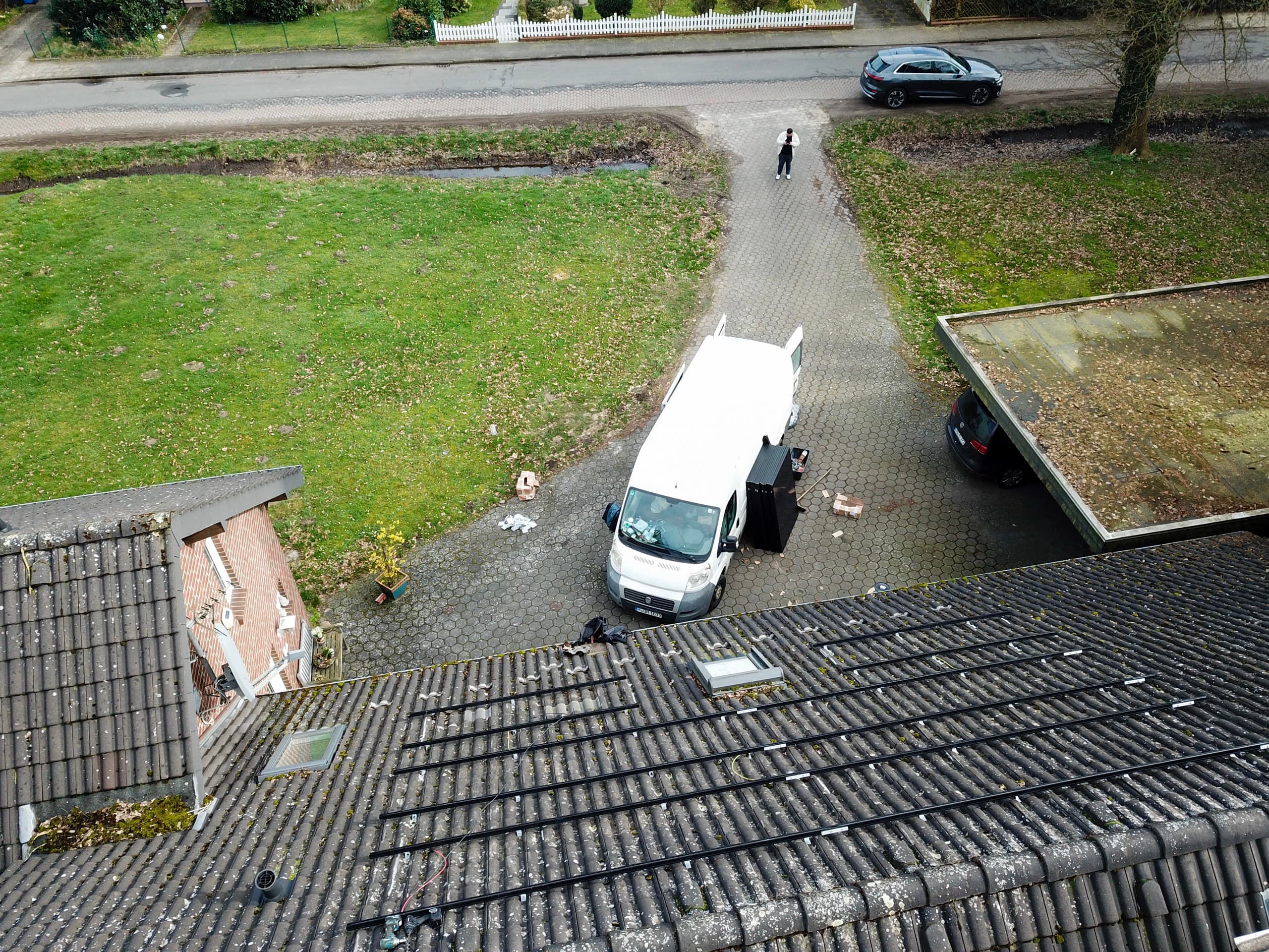 Drohnenaufnahme einer Baustelle: Montageschienen für Photovoltaikmodule liegen auf dem Dach, der Transporter des Betriebs steht im Hof