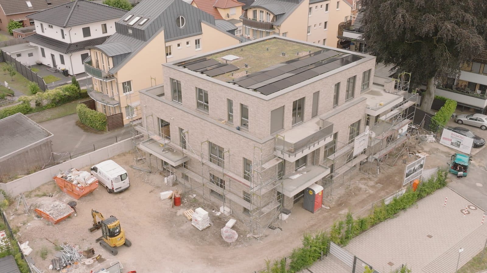 Drohnenaufnahme einer Baustelle der Alfa Projektbau GmbH: Mehrfamilienhaus im Rohbau mit Gerüst, Bagger und Baucontainern