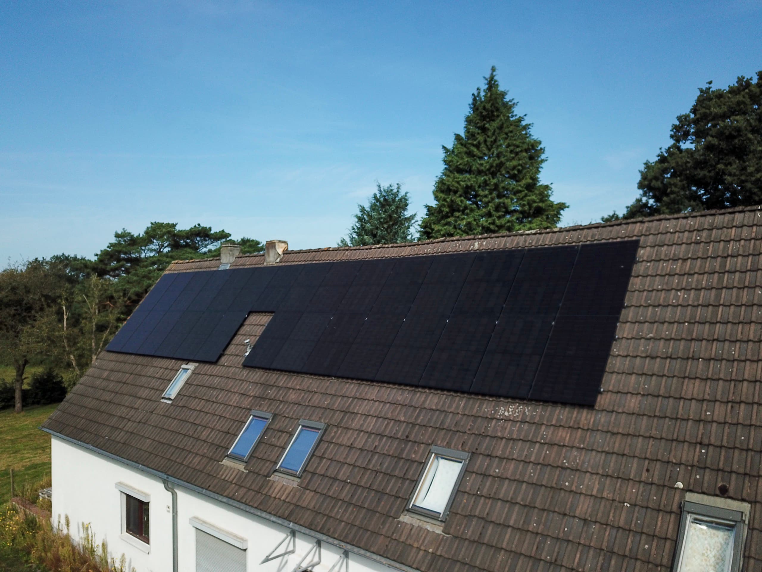 Photovoltaikmodule auf dem Dach eines Wohnhauses vor blauem Himmel, Drohnenaufnahme