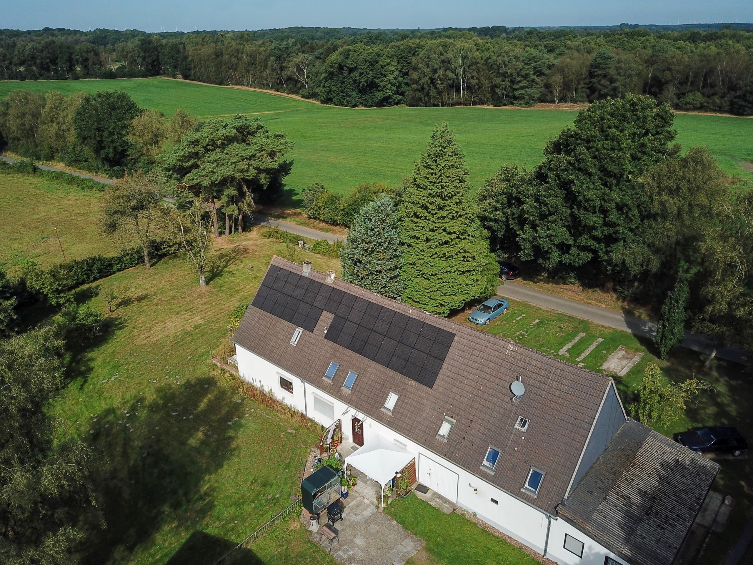 Drohnenaufnahme eines Wohnhauses mit Photovoltaikanlage zwischen Feldern und Waldrand in Norddeutschland